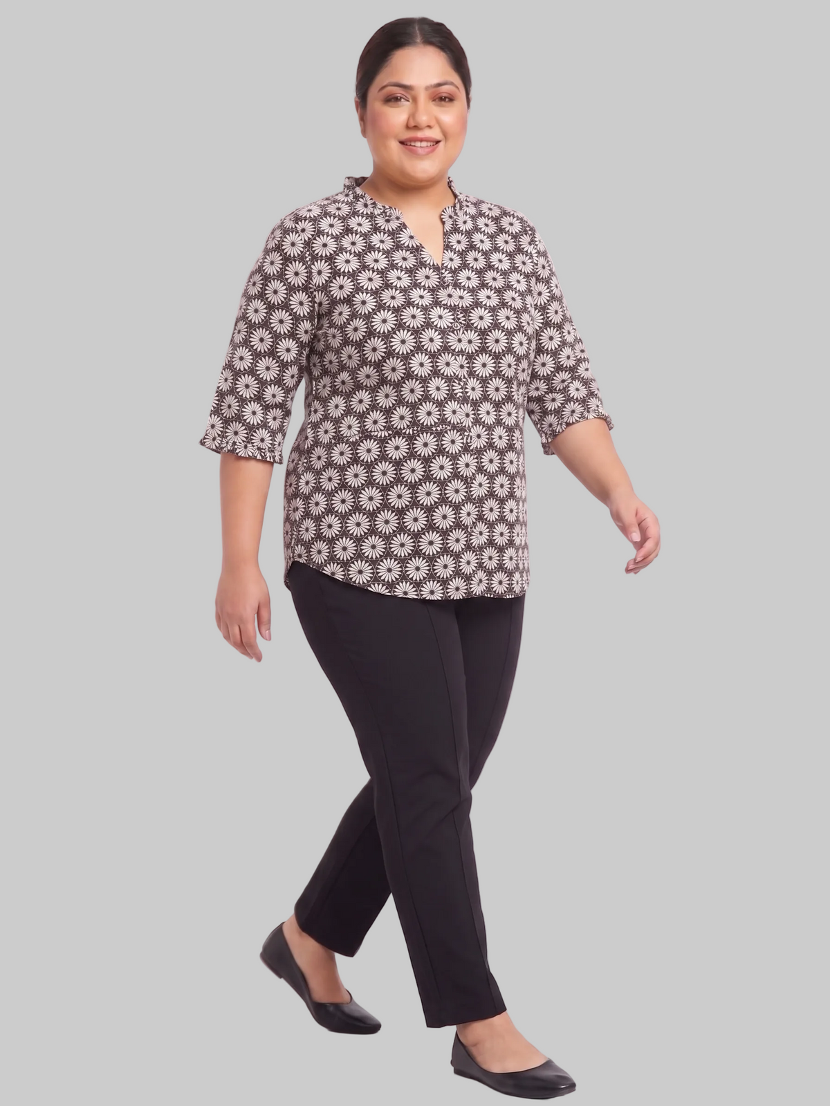 Woman wearing a patterned top and black pants on a white background