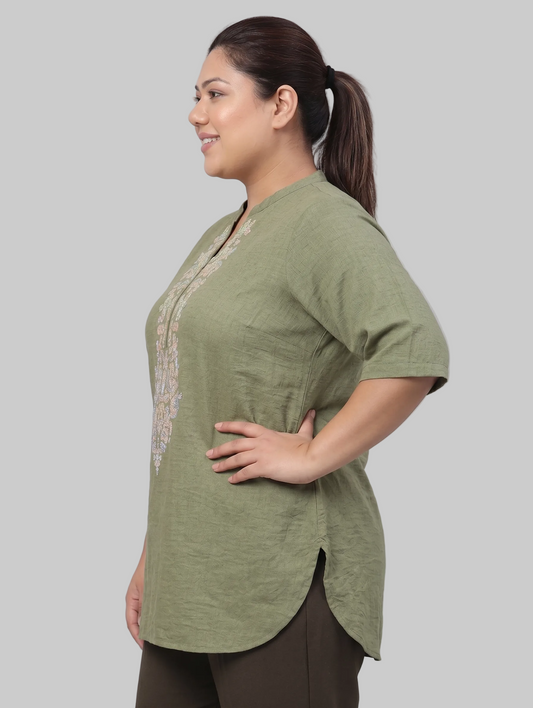 Woman wearing a green top with lace details on a gray background