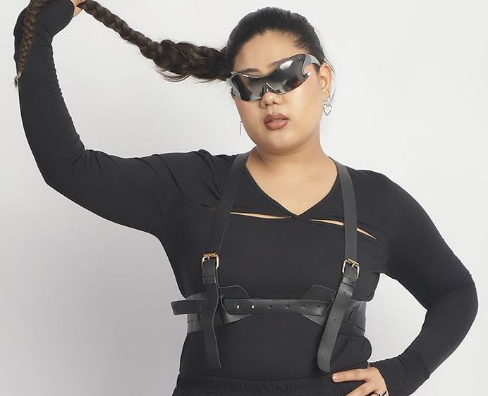 Person wearing a black outfit with suspenders against a white background